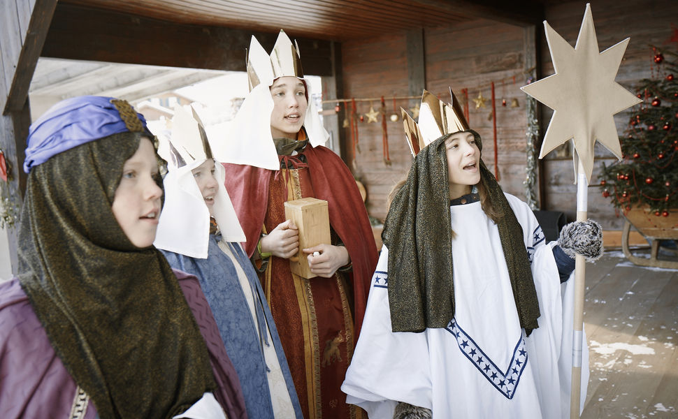 Vier Sternsinger singen. Sie haben eine Spendendose und einen Stern dabei.