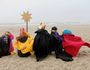 Fünf Sternsinger sitzen mit ihrem Stern am Strand und schauen auf das Meer.
