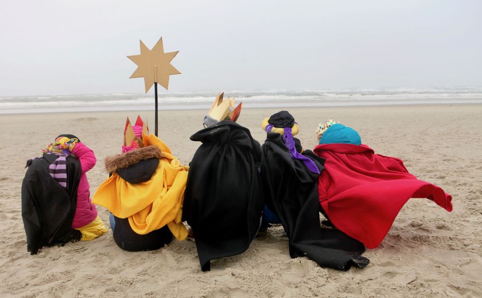Fünf Sternsinger sitzen mit ihrem Stern am Strand und schauen auf das Meer.
