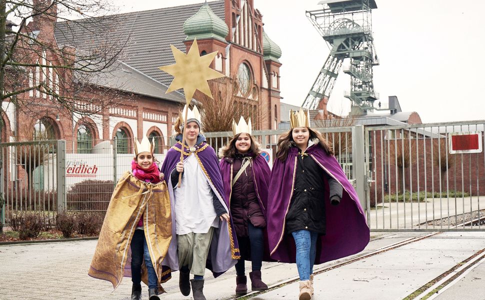 Vier Sternsinger stehen vor einem Förderturm